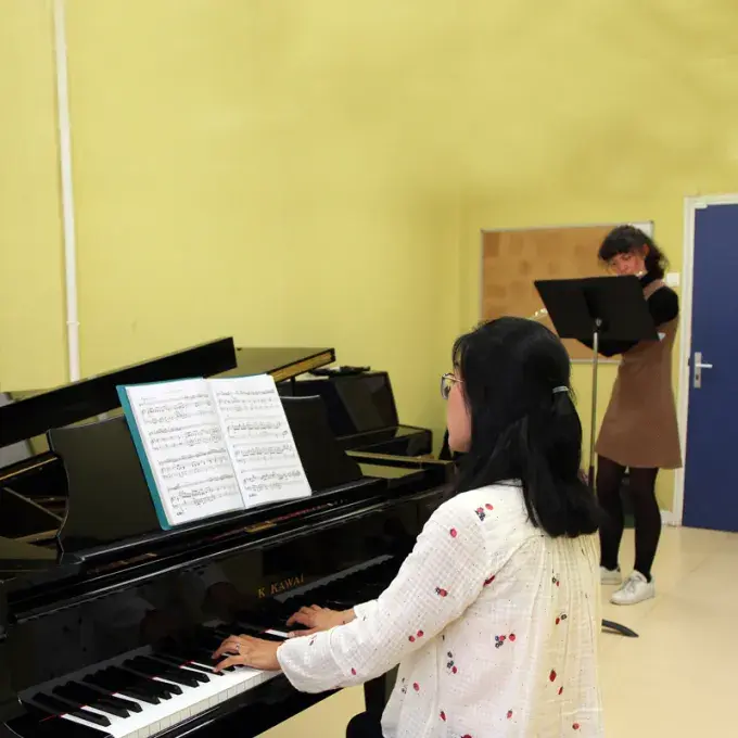 Photo montrant une jeune femme jouant du piano en accompagnement d'une jeune femme jouant de la flûte traversière.