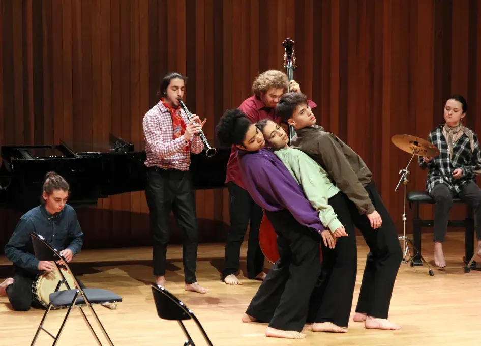 Photo montrant 3 étudiants jouant une scène de théâtre accompagnés par d'autres étudiants jouant de la musique.