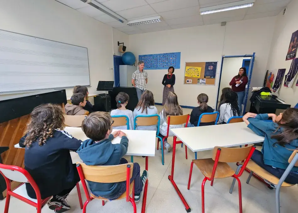 Photo montrant deux adultes debout s'adressant à des élèves assis dans une salle de ocurs de musique