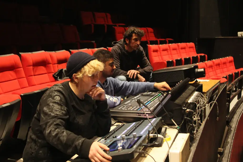 Photo montrant 3 agents technique du conservatoire actionnant les boutons d'une console numérique pour régler le son et la lumière dans l'auditorium.