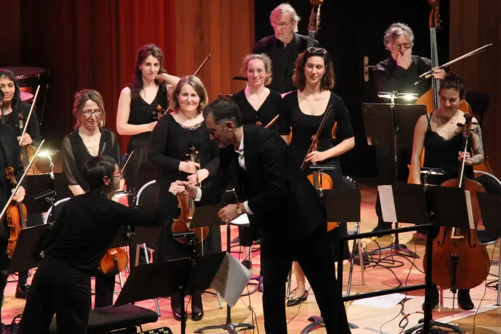 Photo montrant un chef d'orchetsre saluant ses muciennes et musiciens sur scène