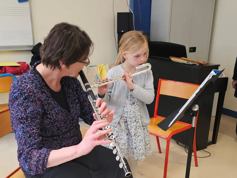 Photo montrant une professeure et une élève jouant de la flûte traversière en suivant une partition.