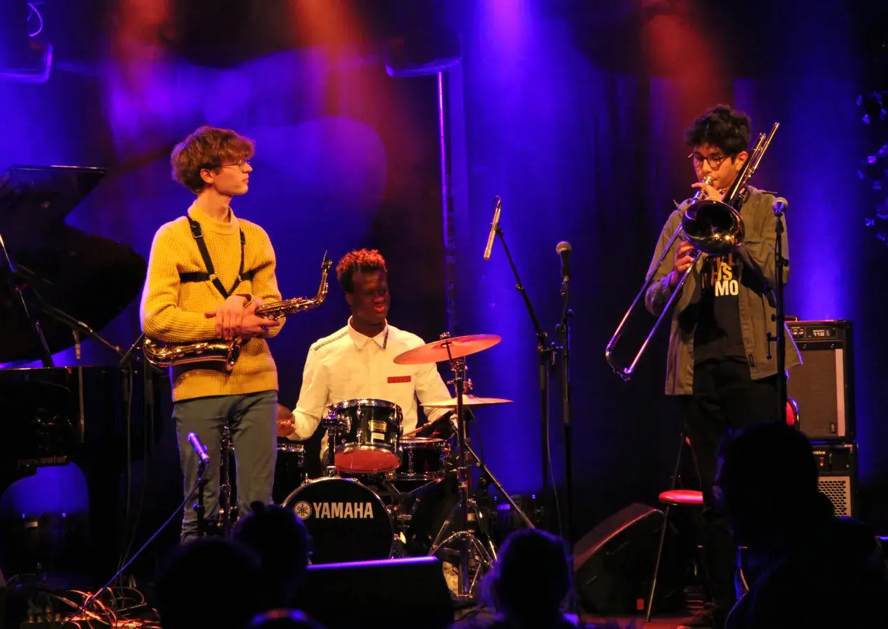 Photo montrant 3 jeunes musiciens de jazz sur scène (saxophone, batterie, trombone)