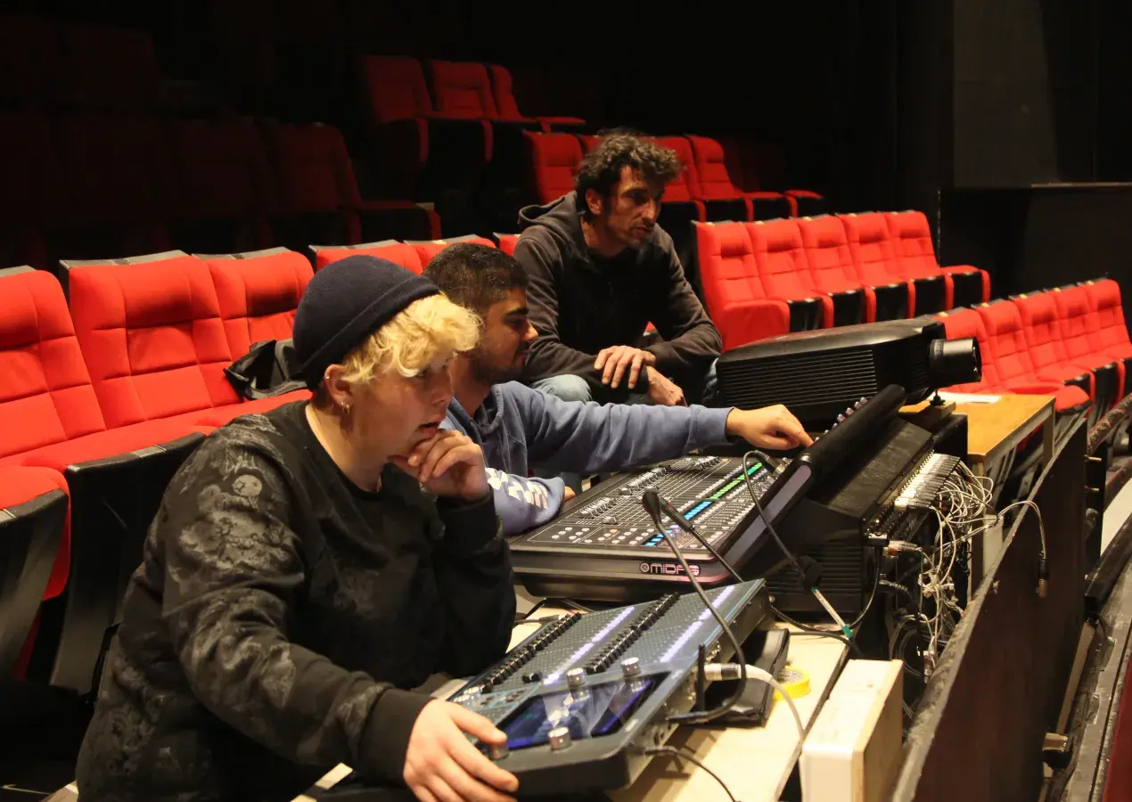 Photo montrant 3 agents technique du conservatoire actionnant les boutons d'une console numérique pour régler le son et la lumière dans l'auditorium.