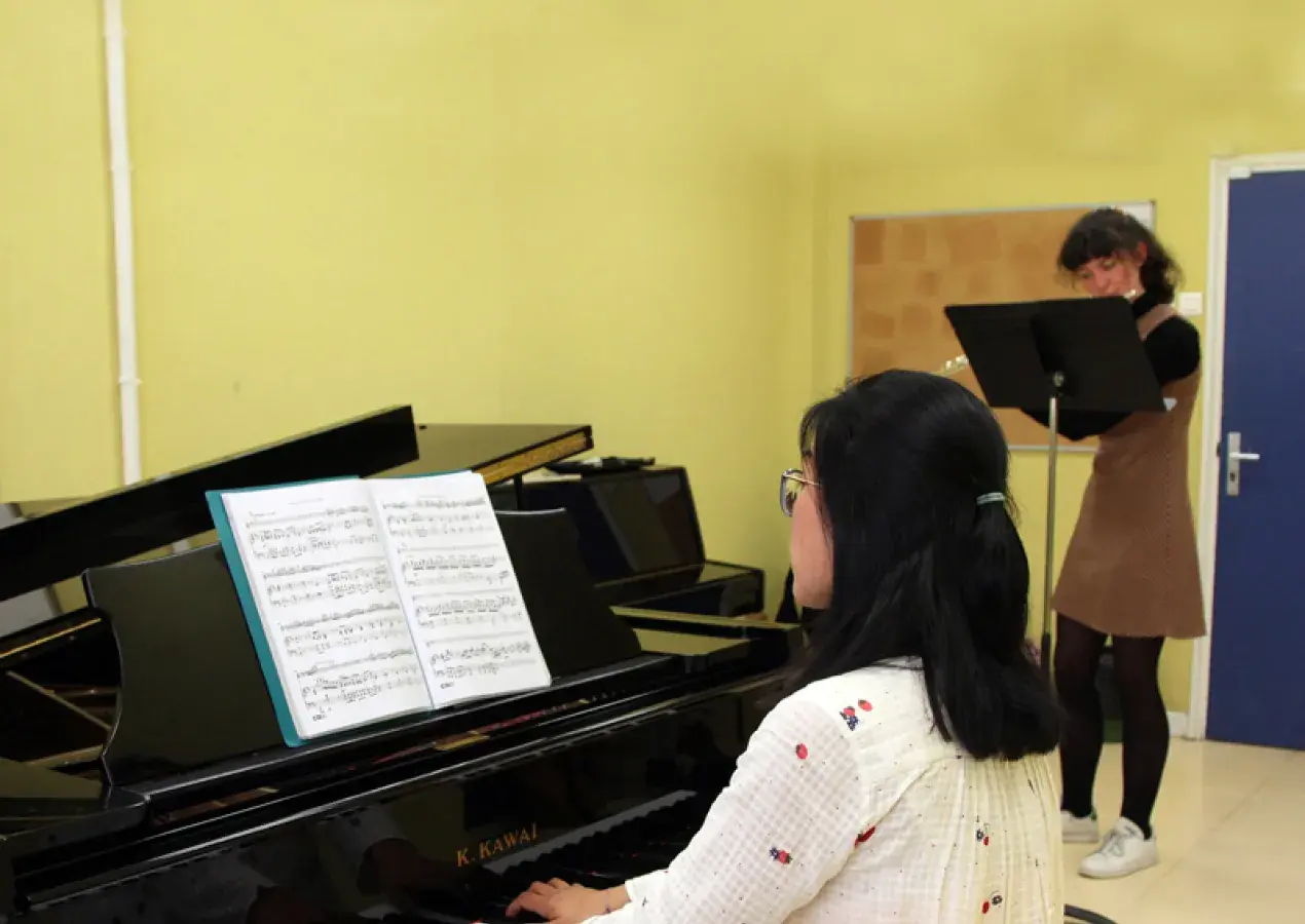 Photo montrant une jeune femme jouant du piano en accompagnement d'une jeune femme jouant de la flûte traversière.