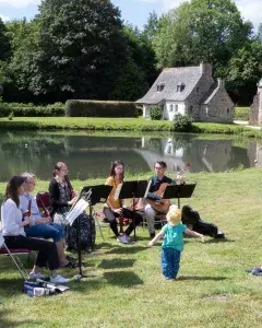 Photo du Brin classik 2022 montrant un groupe de flûtistes dans un jardin jouant de la musique devant des spectacteurs assis dans l'herbe