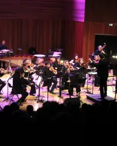Photo montrant des musiciennes et musiciens jouant en orchestre sur une scène sous la direction d'un chef