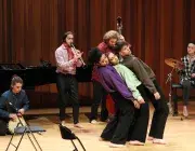 Photo montrant 3 étudiants jouant une scène de théâtre accompagnés par d'autres étudiants jouant de la musique.
