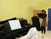 Photo montrant une jeune femme jouant du piano en accompagnement d'une jeune femme jouant de la flûte traversière.