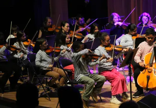 Photo montrant de jeunes instrumentistes à cordes vêtus d'une marinière jouant de la musique sur une scène.