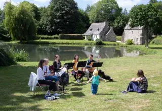 Photo du Brin classik 2022 montrant un groupe de flûtistes dans un jardin jouant de la musique devant des spectacteurs assis dans l'herbe