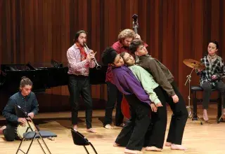Photo montrant 3 étudiants jouant une scène de théâtre accompagnés par d'autres étudiants jouant de la musique.