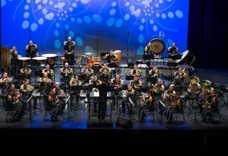 Photo montrant de nombreux musiciens portant un uniforme en concert sur une scène