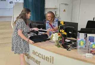 Photo montrant 2 personnes échangeant un instrument à une borne d'accueil