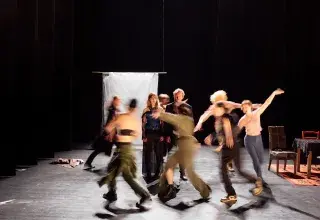 Photo montrant des comédiennes et comédiens courant en cercle autour de 2 personnes sur une scène