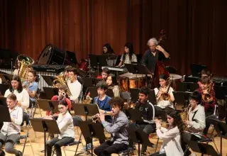 Image montrant des élèves instrumentistes (bois cuivres et contrebasse) jouant en ensemble sur une scène.