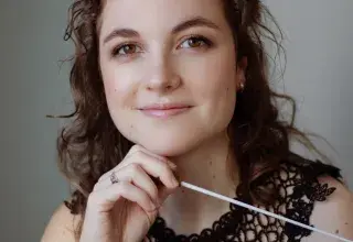 Photo montrant une jeune femme posant avec une baguette de cheffe d'orchestre