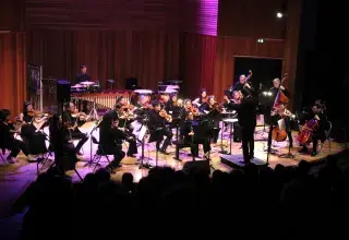 Photo montrant des musiciennes et musiciens jouant en orchestre sur une scène sous la direction d'un chef