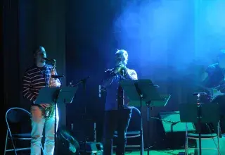 Photo montrant 1 saxophoniste et un trompettiste jouant en concert sur une scène