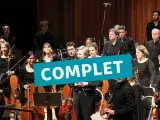 Photo montrant un orchestre sur scène avec un texte indiquant "complet"