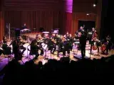 Photo montrant des musiciennes et musiciens jouant en orchestre sur une scène sous la direction d'un chef